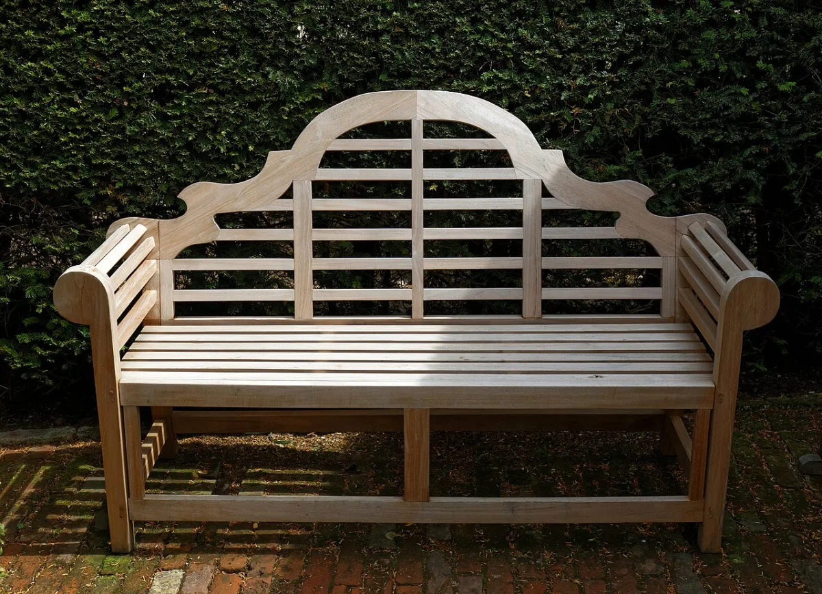 Houten tuinbank met sierlijke rugleuning voor een groene heg
